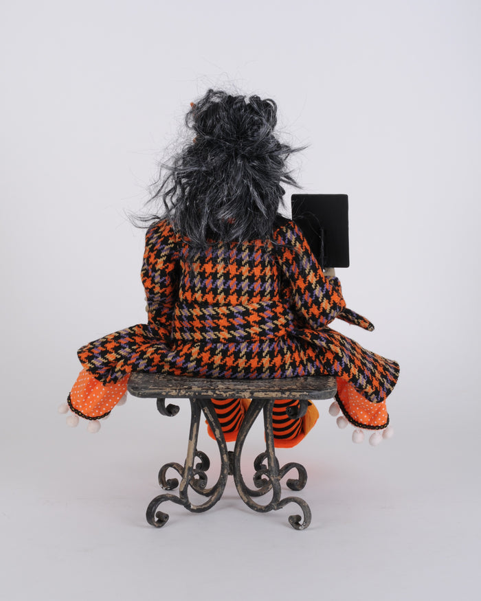 Person wearing a houndstooth coat with orange and black pattern sitting on a chair.
