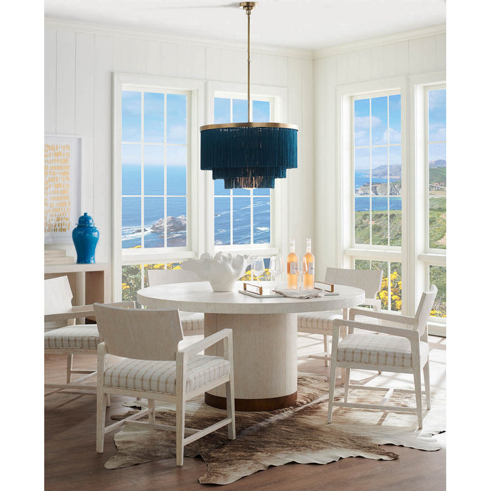 Chandelier with a layered dark blue fringe shade and brass hardware mounted above a white round dining table in a bright