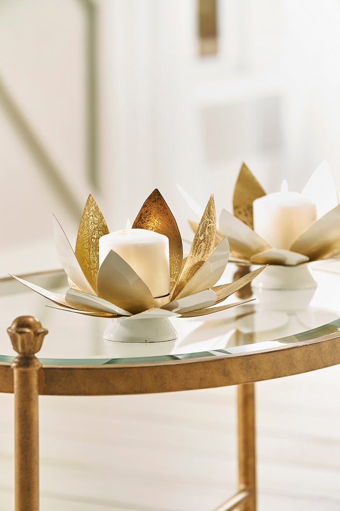 Decorative candle holders with gold leaf design on a glass table.
