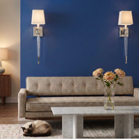 A staged living room scene with a beige upholstered sofa against a deep blue wall, two matching wall sconces, a marble coffee table with flowers, and a cat sleeping on the floor.