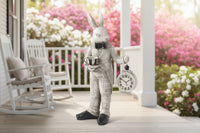 A decorative figurine of a gray and black rabbit wearing a suit, holding a clock in its left hand and a cup in its right hand.