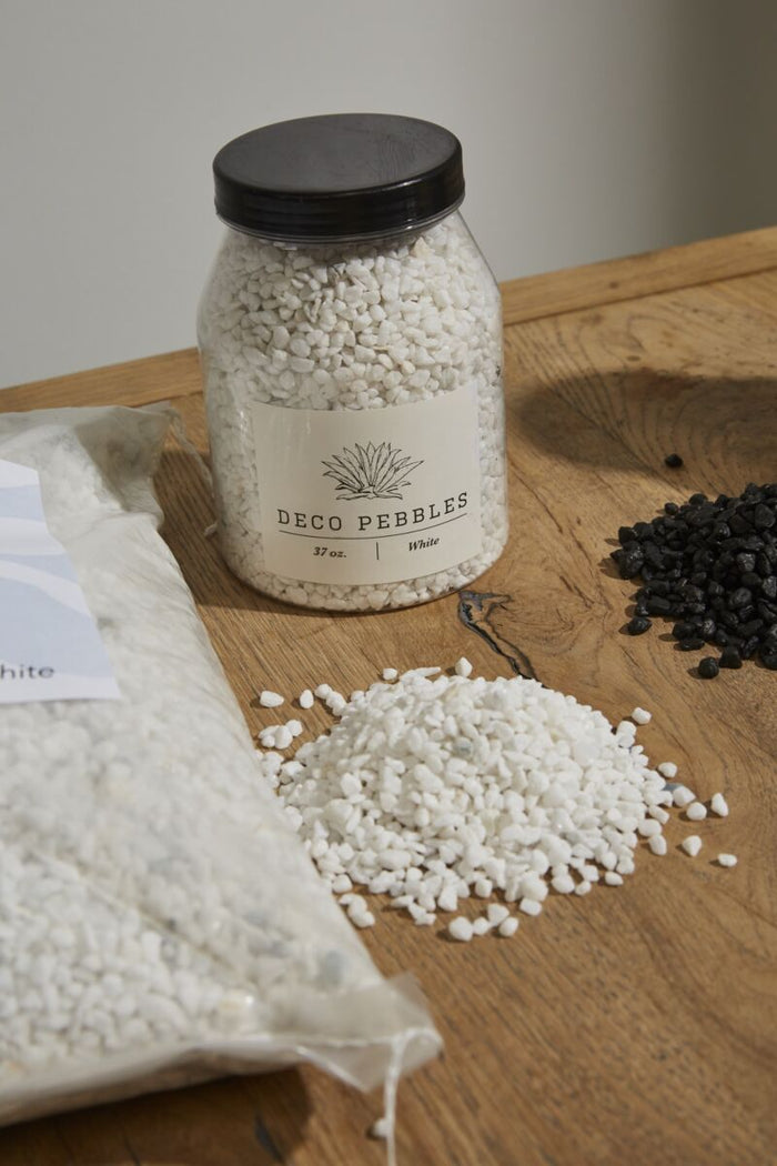 Jar of Deco Pebbles on a wooden surface with white and black pebbles.