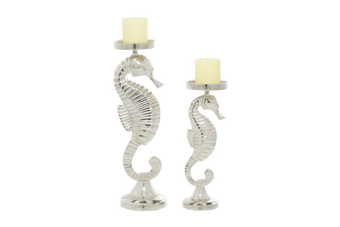 Silver metal seahorse candle holders with cream pillar candles atop round bases, decorative curved bodies against white