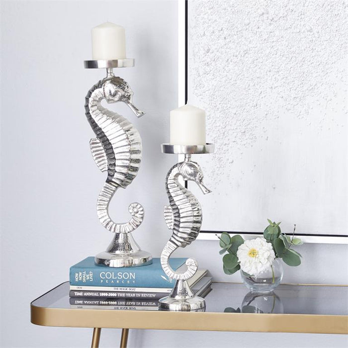 Silver seahorse candle holders with white pillar candles on a glass-top table, chrome accents, decorative books, and a white
