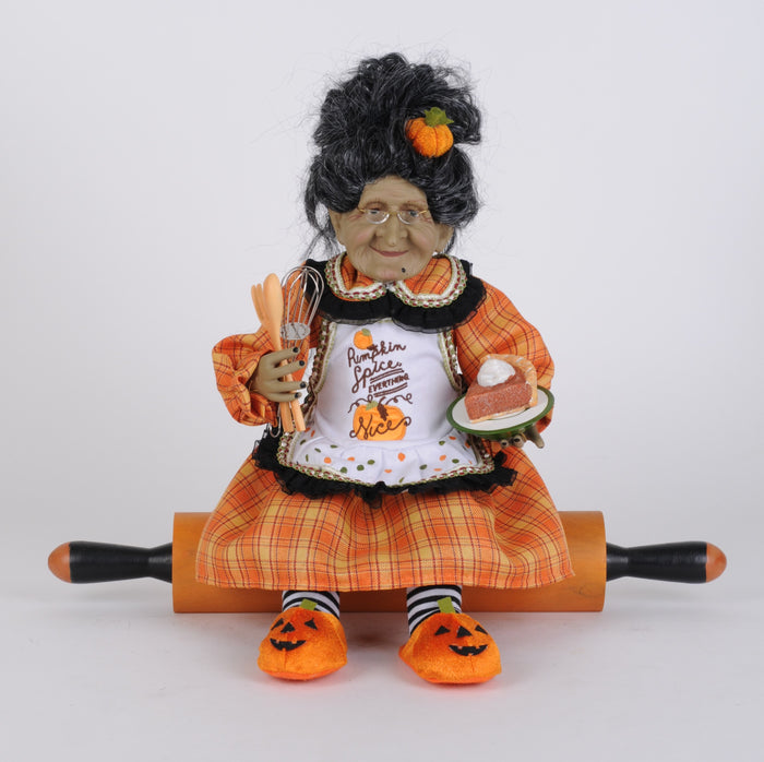Decorative doll in Halloween-themed outfit sitting on a rolling pin.