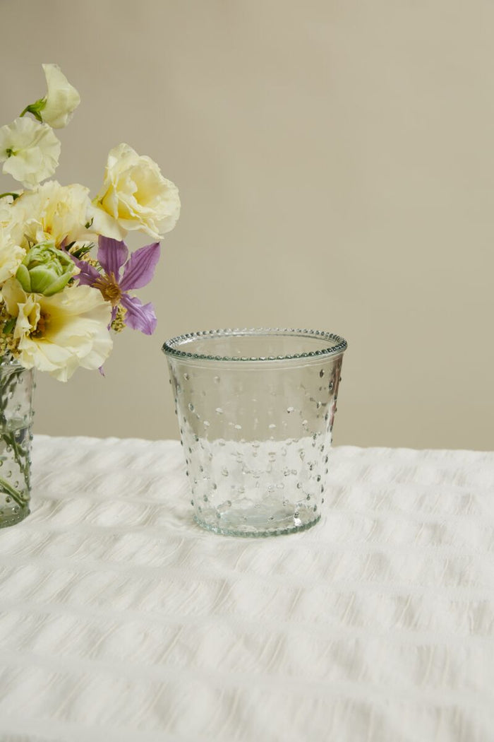 Clear glass vase with textured surface on a white surface, next to a bouquet of flowers.