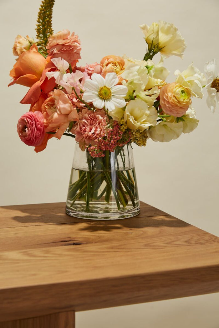 Clear vase with colorful flowers on a wooden surface