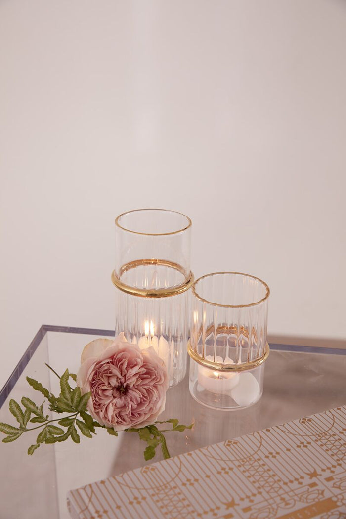 Decorative candles with gold accents on a reflective surface with a light background