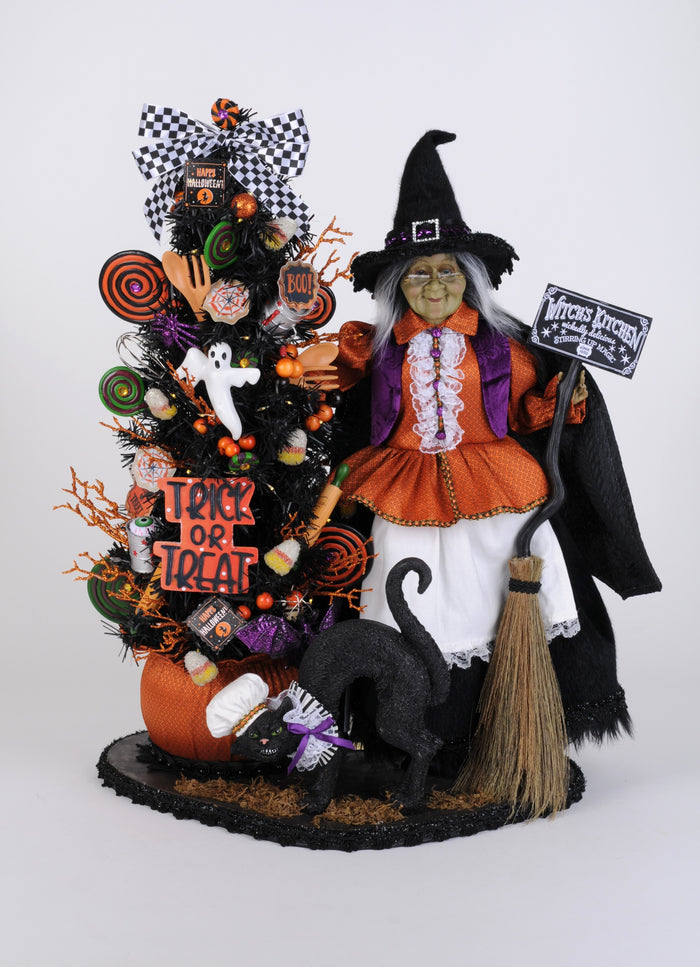 Halloween-themed display with a witch figurine, black cat, and decorated tree on a white background
