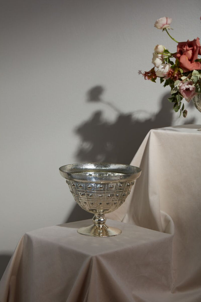 Silver goblet on a table with a white cloth and flowers against a gray wall