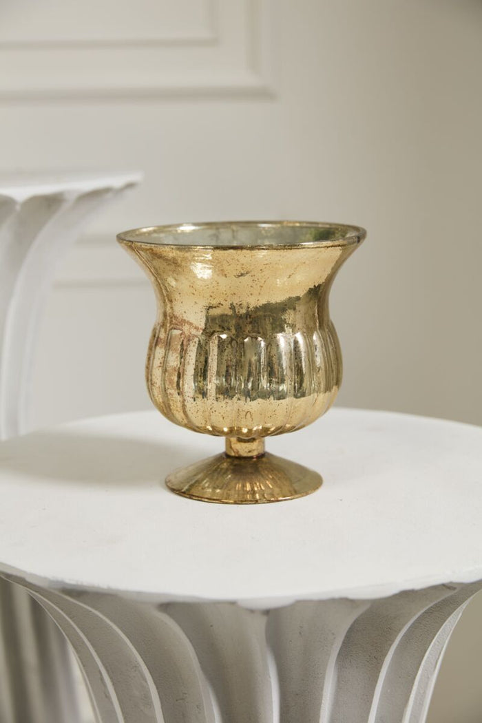 Gold glass vase on a white surface with a neutral background