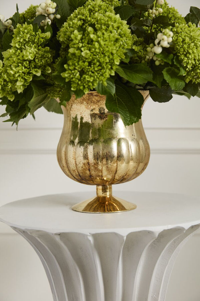 Gold vase with green flowers on a white surface