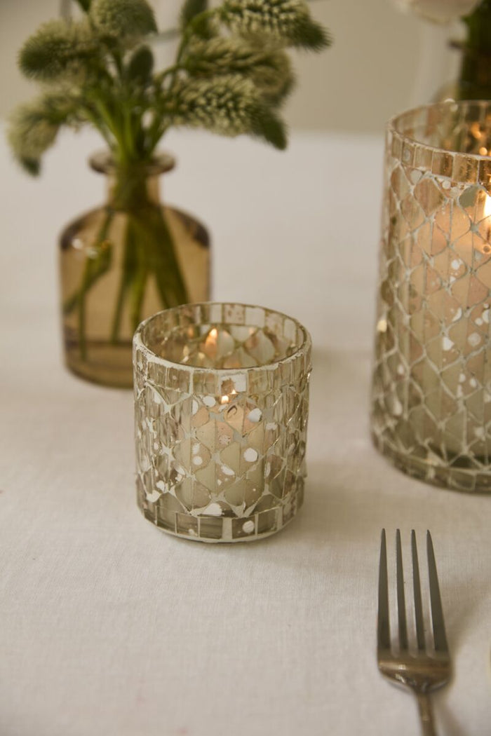 Decorative glass candle holders with a vase of flowers and a fork on a white surface.