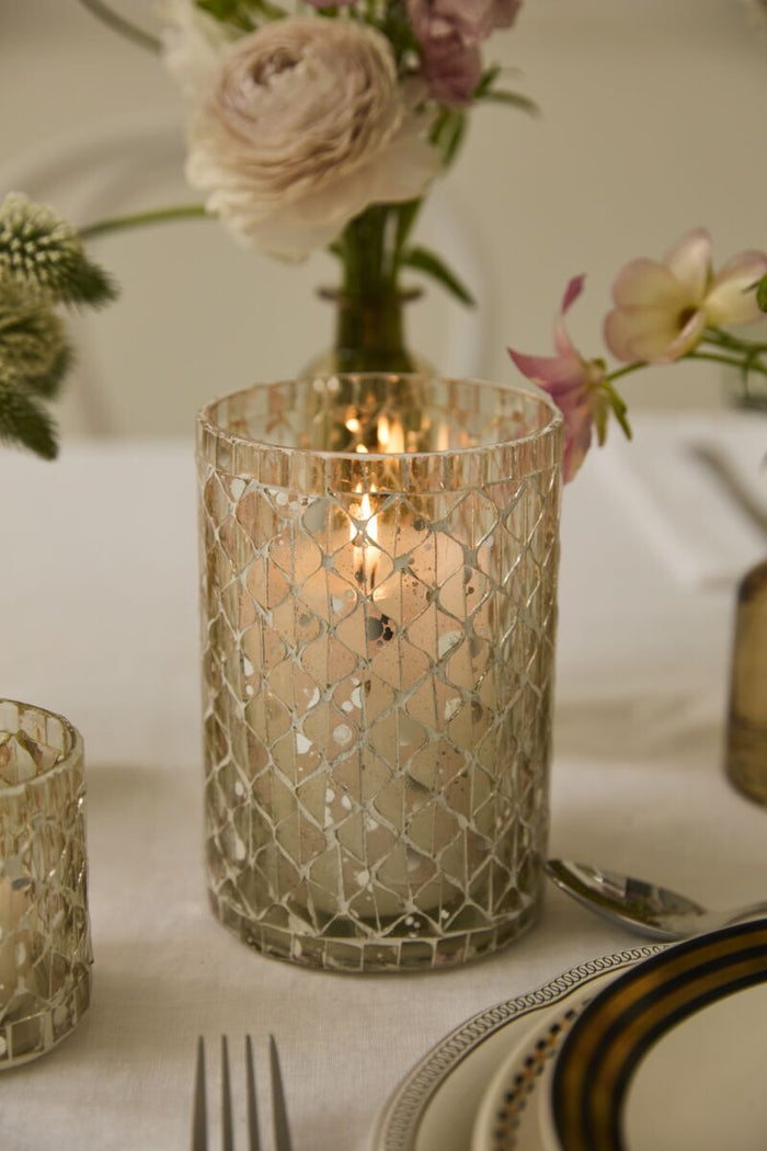 Decorative glass candle holder on a table with flowers and cutlery in the background