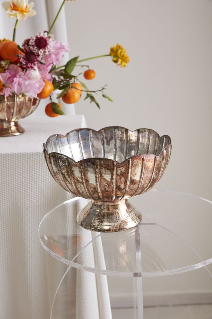 Decorative silver bowl on a clear glass table with flowers in the background