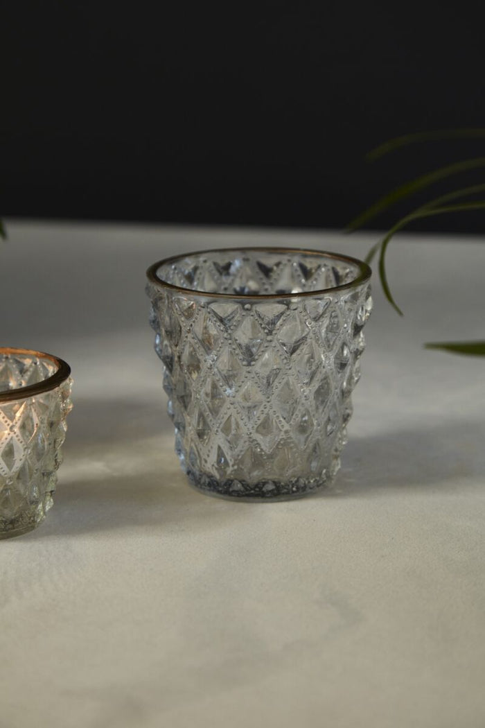 Two textured glass candle holders on a light surface with a dark background