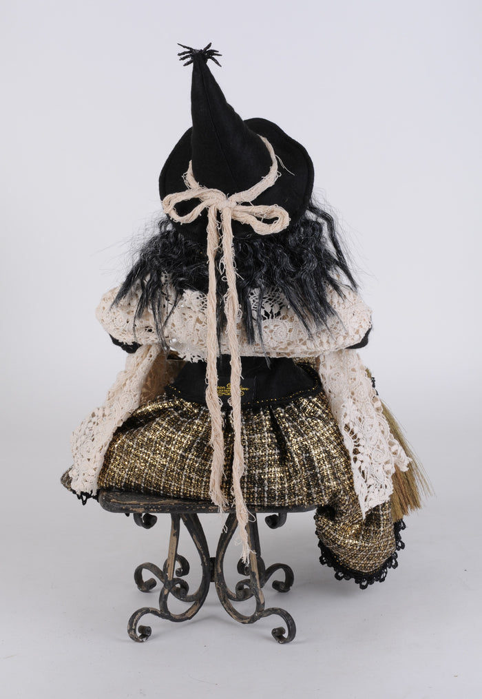 Decorative witch figure with a black hat and long scarf on a white background