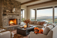 Decorative owl figurine wearing a witch hat on a fireplace mantle in a living room scene in Tennessee. The setting has a khaki sofa with decorative pillows, a neutral mid-century modern accent chair, a wood coffee table with books, candles on a tray. There is also a view of the mountains and lake.