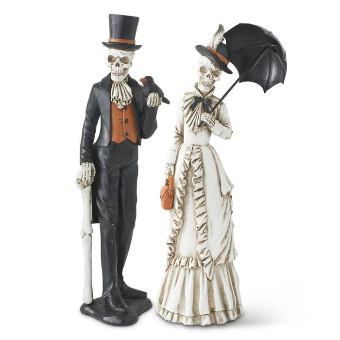 Set of two resin skeleton figures: a man in a black suit with top hat and cane; a woman in a white bridal dress with parasol.