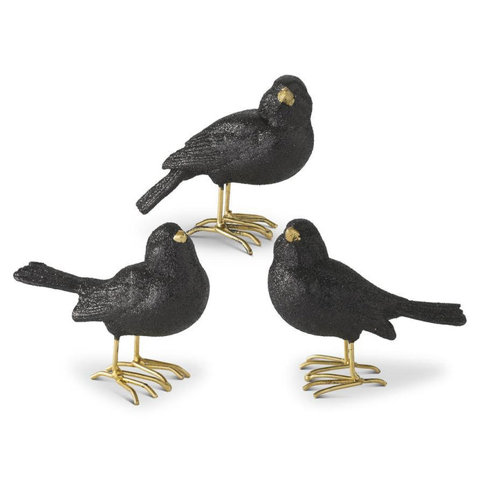 Three black bird figurines with gold feet on a white background