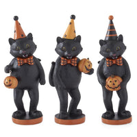 Three black cat figurines wearing Halloween hats and holding pumpkins on a white background