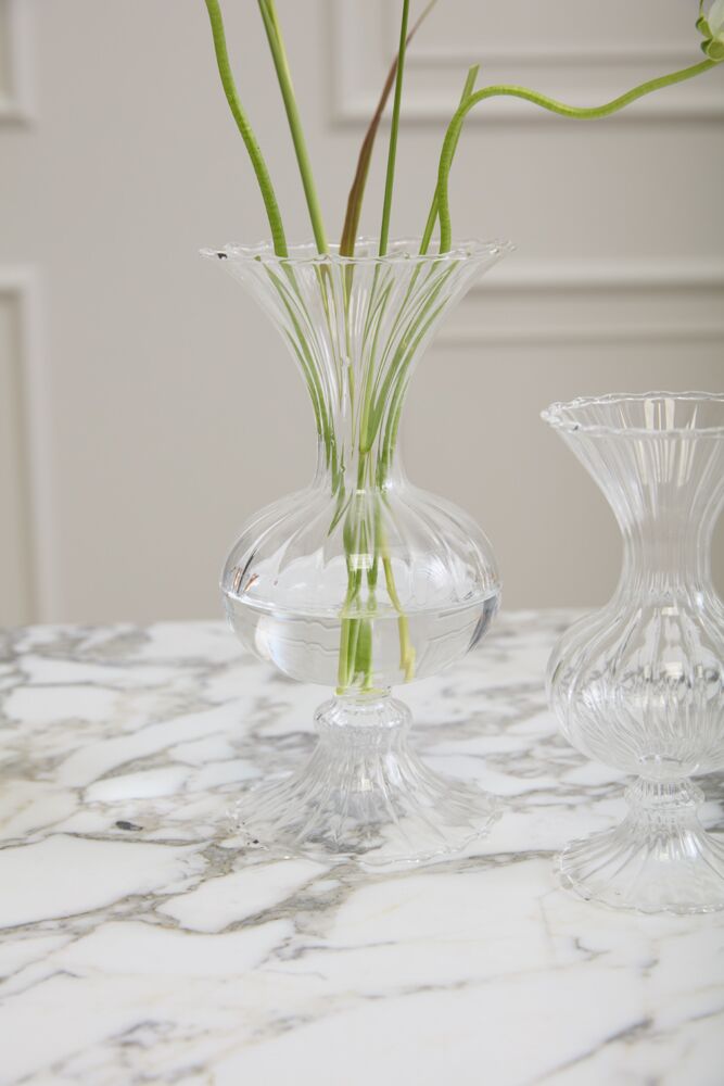 Clear glass vase with green stems on a marble surface