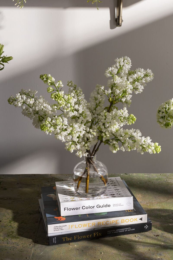 Floral arrangement in a clear vase on top of books with a neutral background