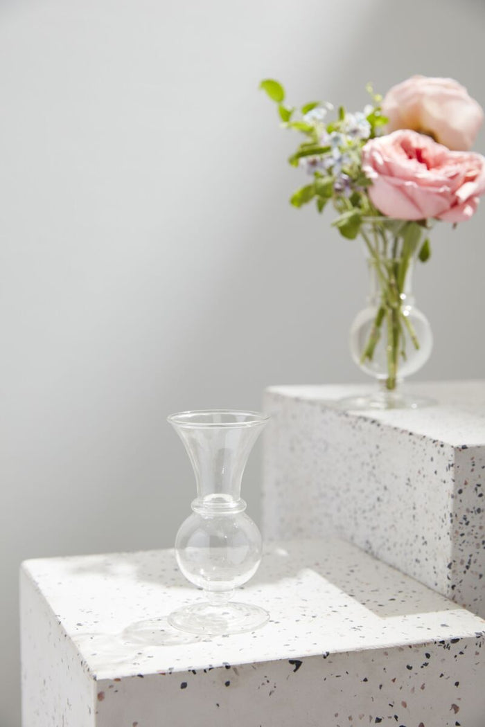Clear glass vase with flowers on a textured surface against a light gray background