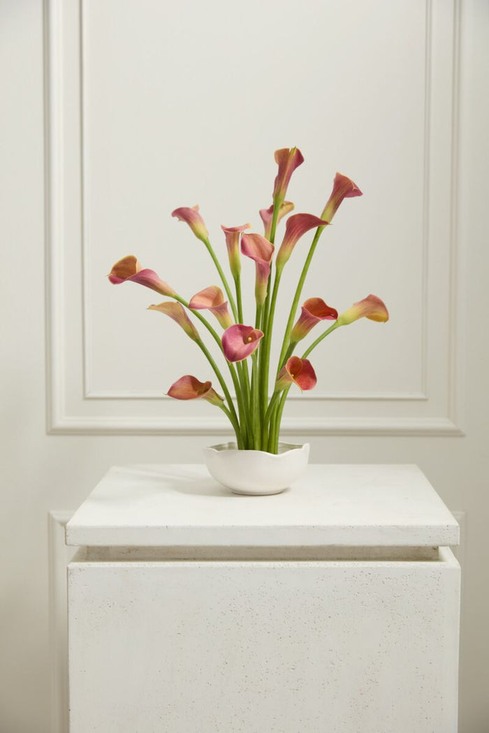 Faux pink calla lilies in a white vase on a white surface with a white paneled wall background