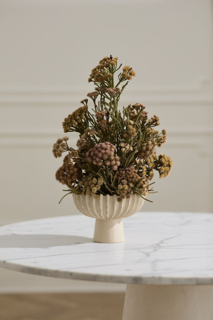 Dried floral arrangement in a beige vase on a marble surface with a neutral background