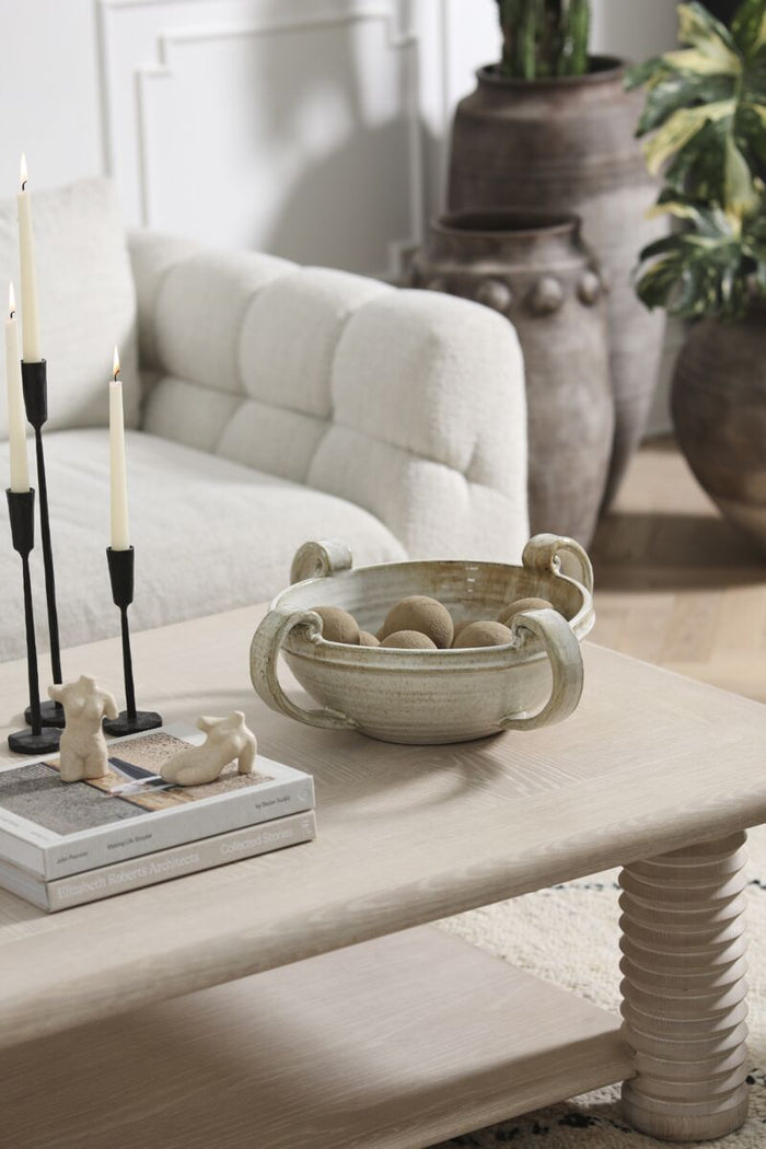 Living room with a coffee table featuring decorative items, a couch, and potted plants.