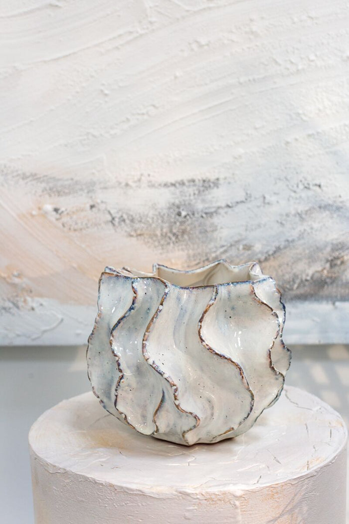 Decorative ceramic vase with wavy patterns on a white pedestal against a textured white background