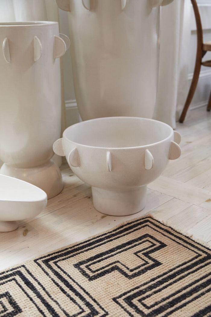 White ceramic bowls with decorative handles on a light wooden floor.