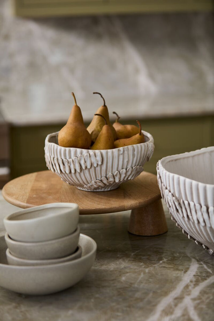 Bowl of pears on a wooden stand with ceramic bowls below on a marble surface