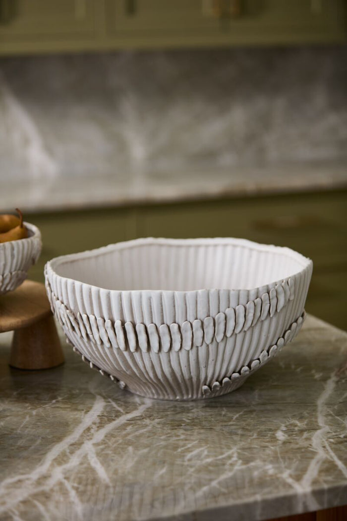 White textured ceramic bowl on a marble countertop with a kitchen setting in the background.