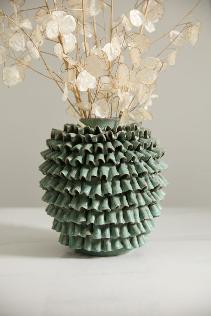 Green textured vase with dried flowers on a light background