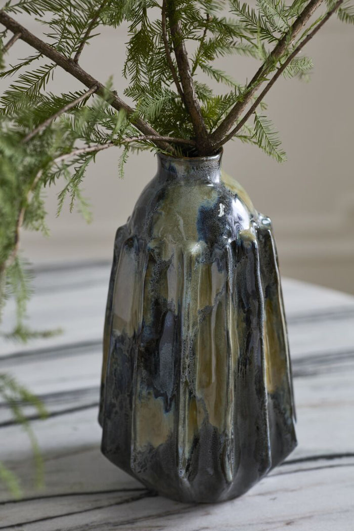 Decorative vase with a unique glaze pattern holding greenery on a wooden surface.