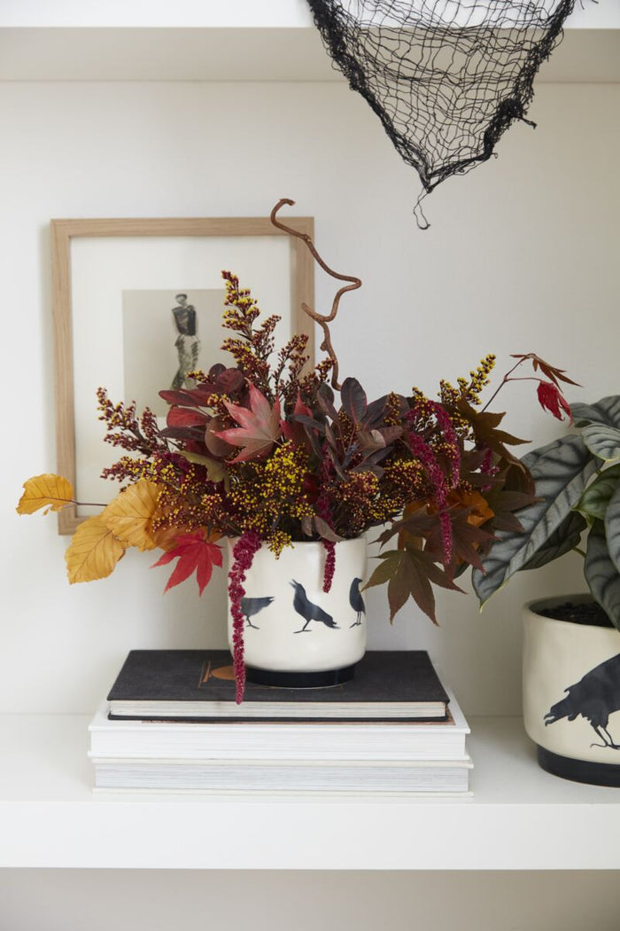 Decorative fall arrangement in a pot with autumn leaves on a shelf.