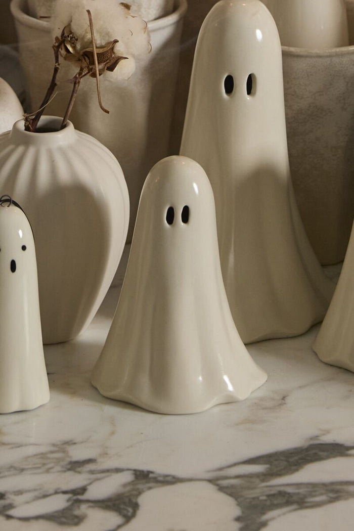 Three small ghost figurines on a surface with pumpkins in the background
