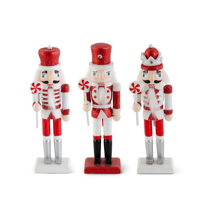Three nutcracker figurines in red and white outfits with candy cane hats on a white background.