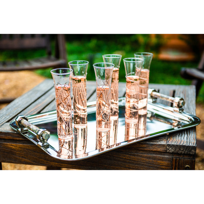 Set of six clear glasses with rose gold liquid on a silver tray outdoors.