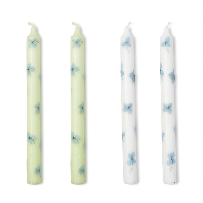 A set of four taper candles with hydrangea petal decals, two in white and two in a light green color, displayed side by side.