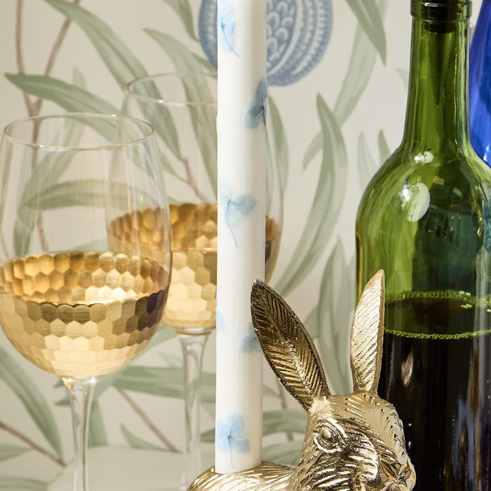 Two tapered white candles with blue hydrangea petal decals, set in a gift box with gold goblet-style glasses, green wine