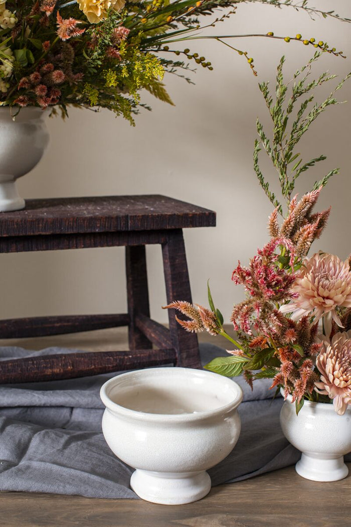 Decorative floral arrangements in white vases on a wooden surface with a neutral background.
