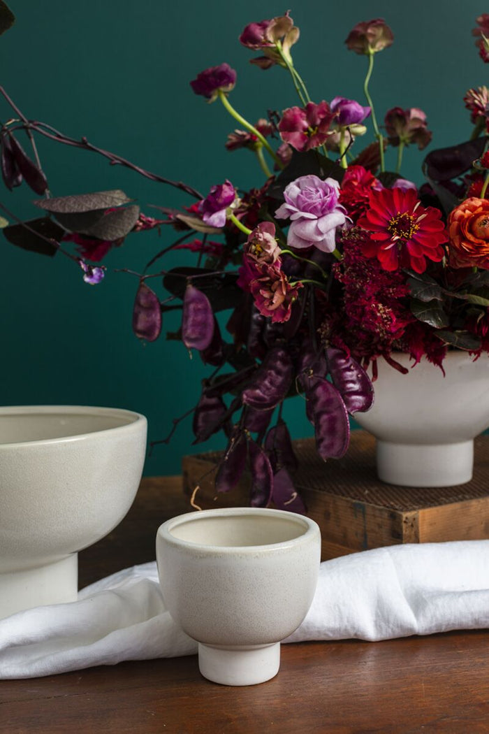 Floral arrangement with a white ceramic vase on a wooden surface against a teal background
