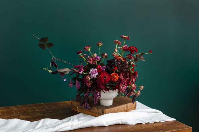 Bouquet of flowers in a white vase on a wooden table with a dark green background