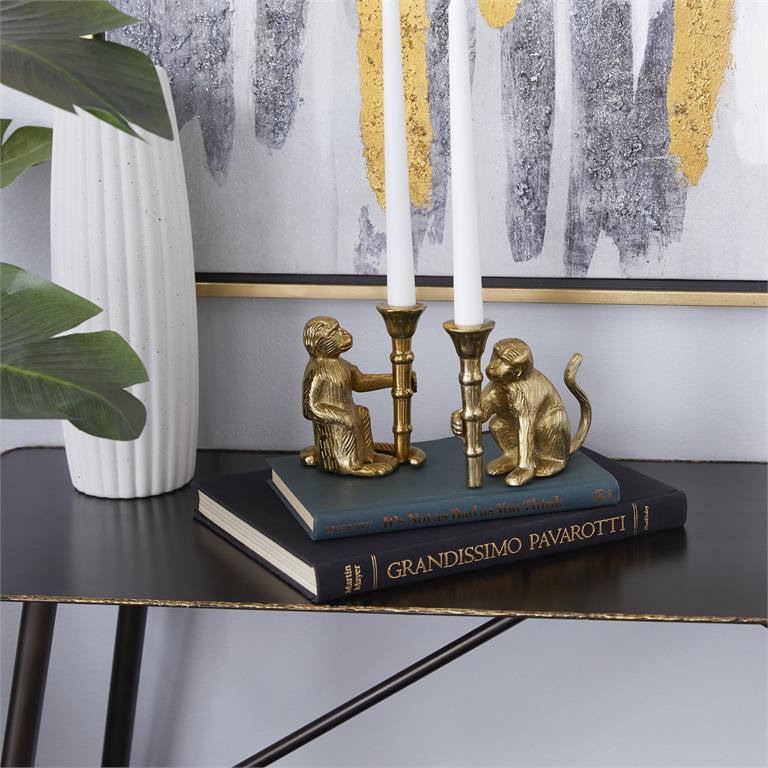 Gold aluminum candle holder set featuring a monkey figure and a seated figure holding candle sticks on a stack of books with