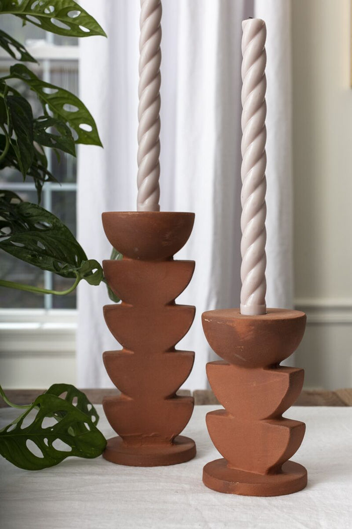 Terracotta Cadwell candle holders with stacked half-sphere shapes, cream twisted candles, on a light table with a plant