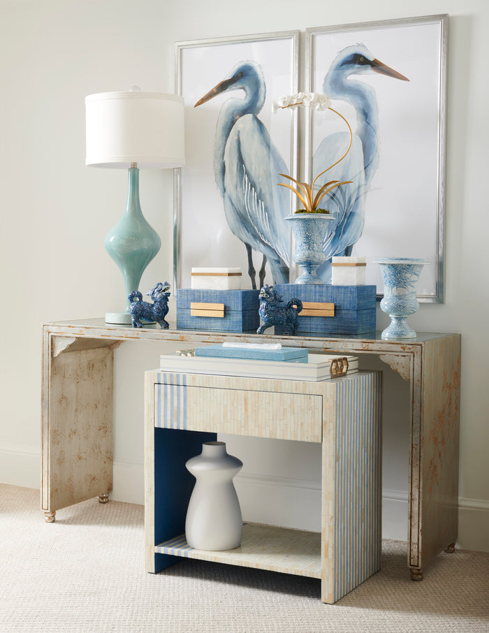 Decorative console table with framed artwork, lamp, and vases against a light wall.