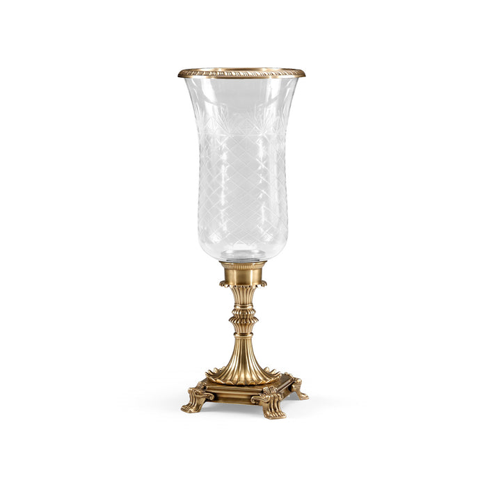 Clear glass hurricane lamp with gold metallic base on a white background